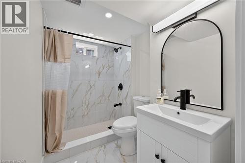 Bathroom featuring a white vanity with integrated sink, black hardware, arched mirror, and recessed lighting - 331 East 17Th Street, Hamilton, ON 