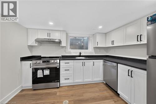 Modern kitchen featuring white shaker cabinetry, dark countertops, wood-finish flooring, stainless steel appliances, and a stainless steel sink with a black faucet - 331 East 17Th Street, Hamilton, ON 
