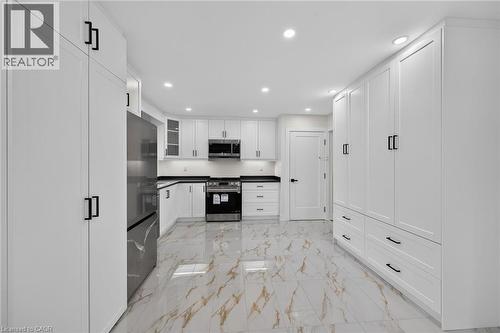 Gleaming tile flooring, extensive white cabinetry with matte black hardware, stainless steel appliances, recessed lighting, and dark countertops - 331 East 17Th Street, Hamilton, ON 