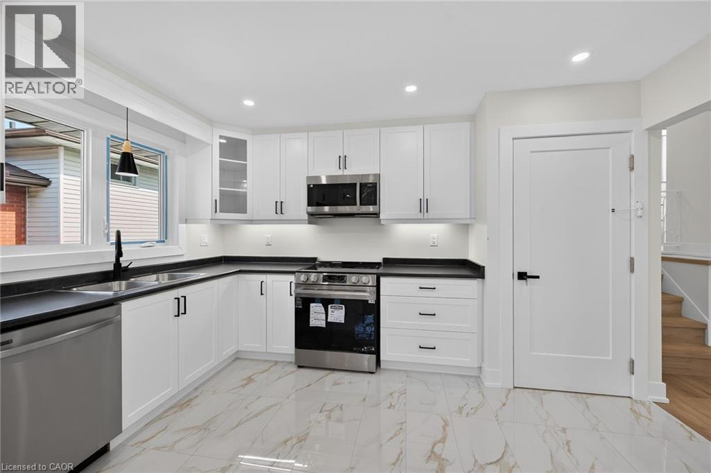 Modern kitchen featuring white cabinetry, dark countertops, stainless steel appliances, and large format floor tiling - 331 East 17Th Street, Hamilton, ON