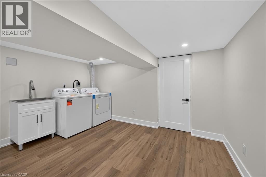 Laundry area featuring a utility sink with cabinet storage, wood-finish flooring, and recessed lighting - 331 East 17Th Street, Hamilton, ON