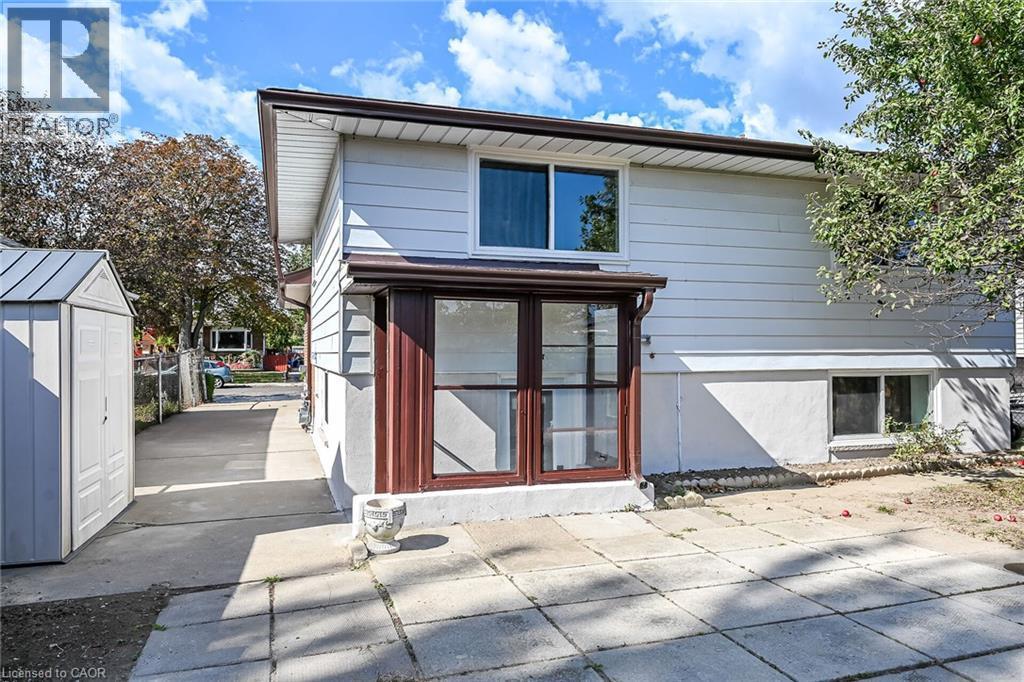 Rear exterior featuring a ground-level patio, private driveway, brown window trim, white siding, and a utility shed - 331 East 17Th Street, Hamilton, ON