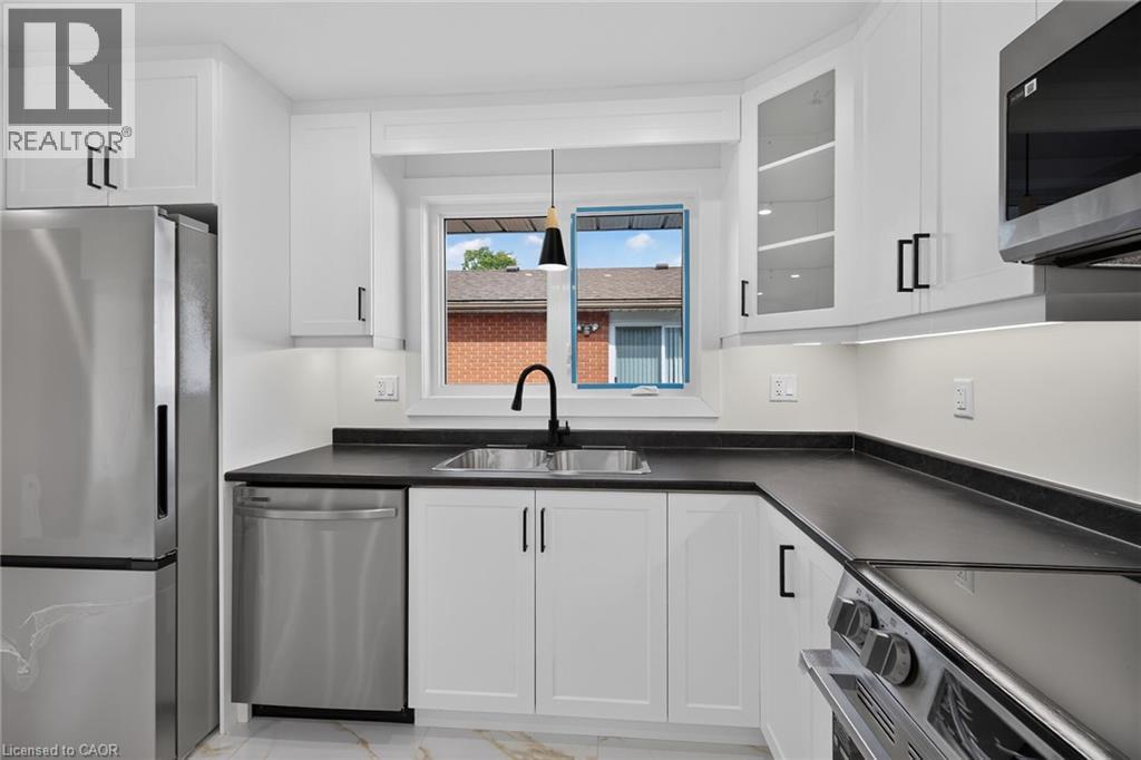 Modern kitchen featuring white cabinetry, stainless steel appliances, dark countertops, a stainless steel sink with a black gooseneck faucet, and a window above the sink - 331 East 17Th Street, Hamilton, ON