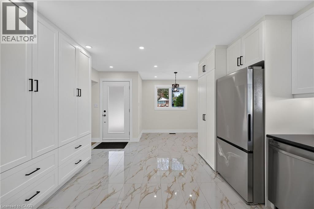 White shaker-style cabinetry with matte black hardware, stainless steel refrigerator, recessed lighting, and a frosted glass panel entry door - 331 East 17Th Street, Hamilton, ON