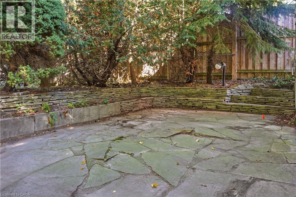 Stone patio with a tiered retaining wall, integrated planter, and mature perimeter trees - 12 Hill Street, Kitchener, ON