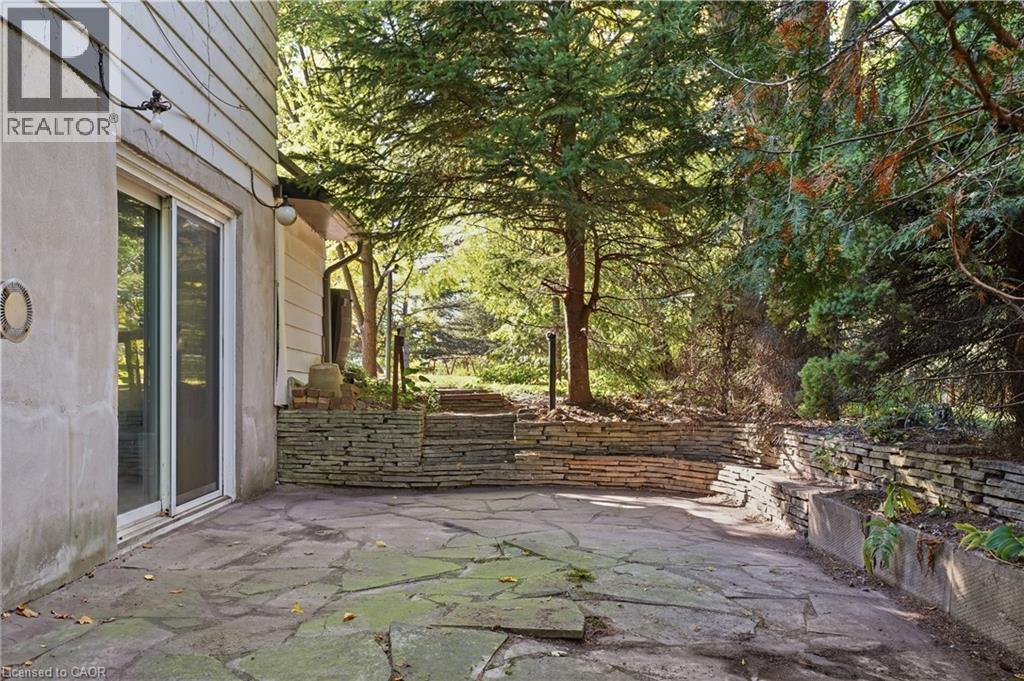 Stone patio with irregular flagstone paving, multiple stacked stone retaining walls, and mature trees - 12 Hill Street, Kitchener, ON