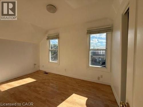 Wood-finish flooring with a white wall finish, featuring two windows with privacy blinds, and a flush mount ceiling light - 1087 Cannon Street E, Hamilton, ON 