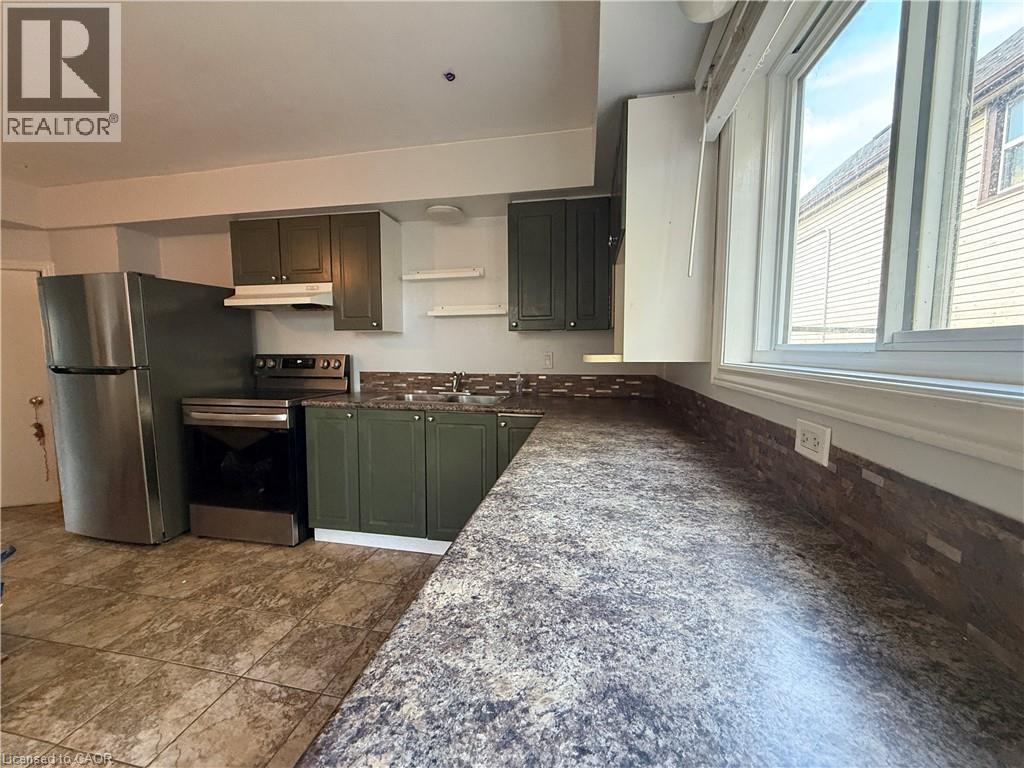 Kitchen featuring durable tile flooring, stainless steel appliances, dark green cabinetry, a mosaic tile backsplash, and a large window - 1087 Cannon Street E, Hamilton, ON
