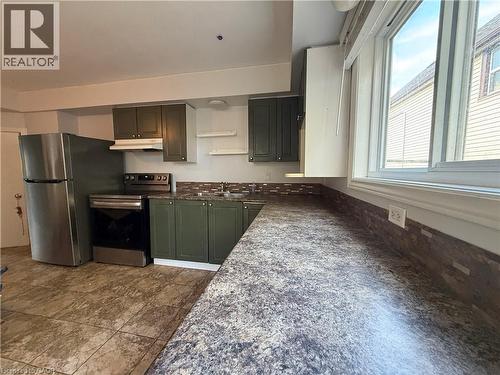 Kitchen featuring durable tile flooring, stainless steel appliances, dark green cabinetry, a mosaic tile backsplash, and a large window - 1087 Cannon Street E, Hamilton, ON 