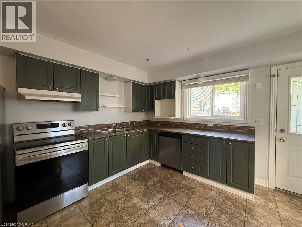 L-shaped kitchen featuring dark green cabinetry, dark countertops, a tiled backsplash, and stainless steel appliances - 1087 Cannon Street E, Hamilton, ON
