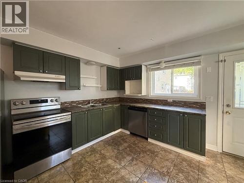 L-shaped kitchen featuring dark green cabinetry, dark countertops, a tiled backsplash, and stainless steel appliances - 1087 Cannon Street E, Hamilton, ON 