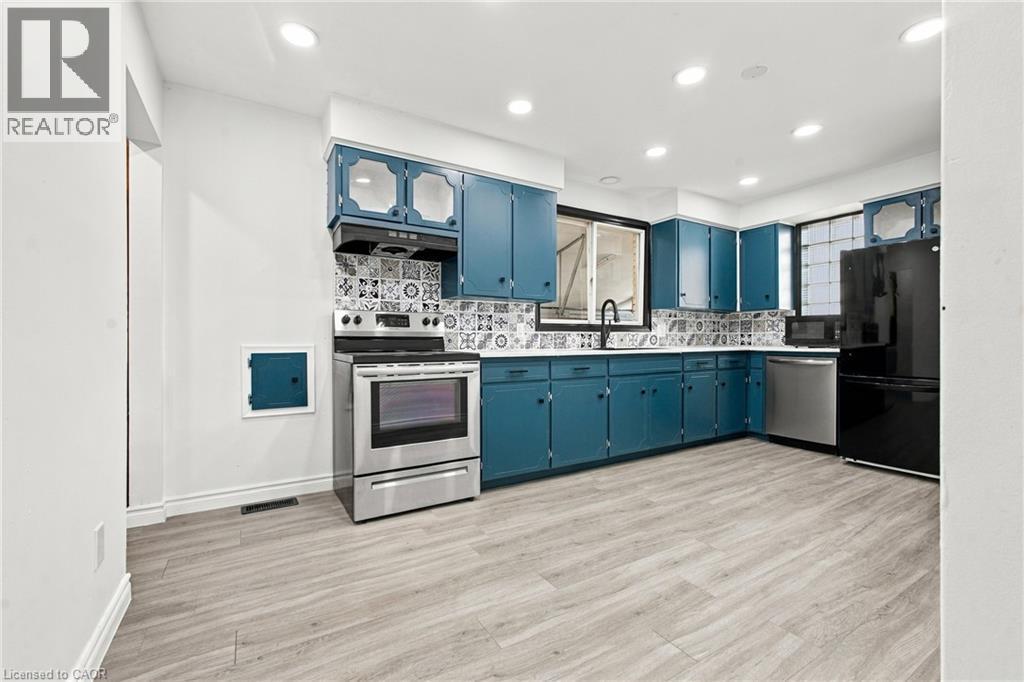 Kitchen featuring teal cabinetry, stainless steel appliances, patterned tile backsplash, wood-finish flooring, and recessed lighting - 246 Hillcrest Road, Cambridge, ON