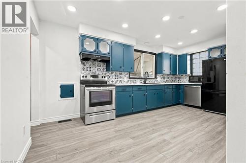 Kitchen featuring teal cabinetry, stainless steel appliances, patterned tile backsplash, wood-finish flooring, and recessed lighting - 246 Hillcrest Road, Cambridge, ON 
