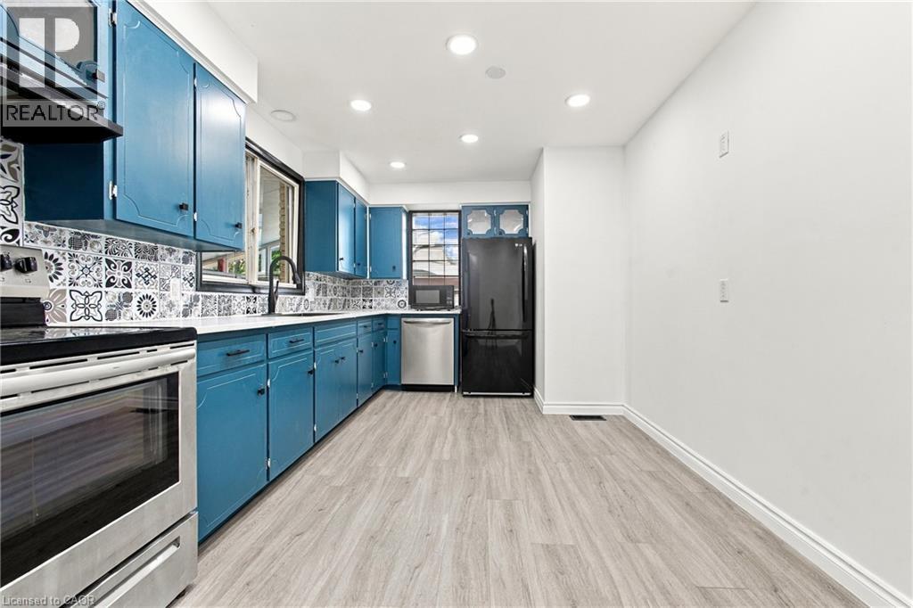 Kitchen featuring blue cabinetry, patterned tile backsplash, stainless steel appliances, wood-finish flooring, and recessed lighting - 246 Hillcrest Road, Cambridge, ON