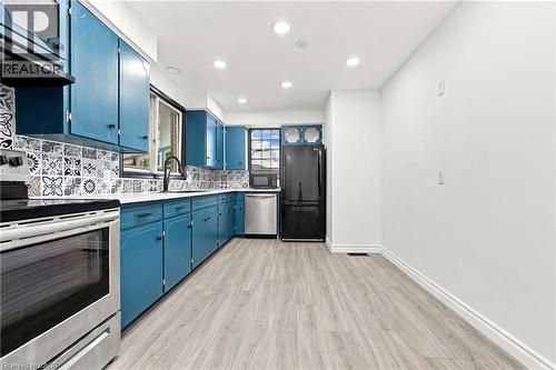 Kitchen featuring blue cabinetry, patterned tile backsplash, stainless steel appliances, wood-finish flooring, and recessed lighting - 246 Hillcrest Road, Cambridge, ON 