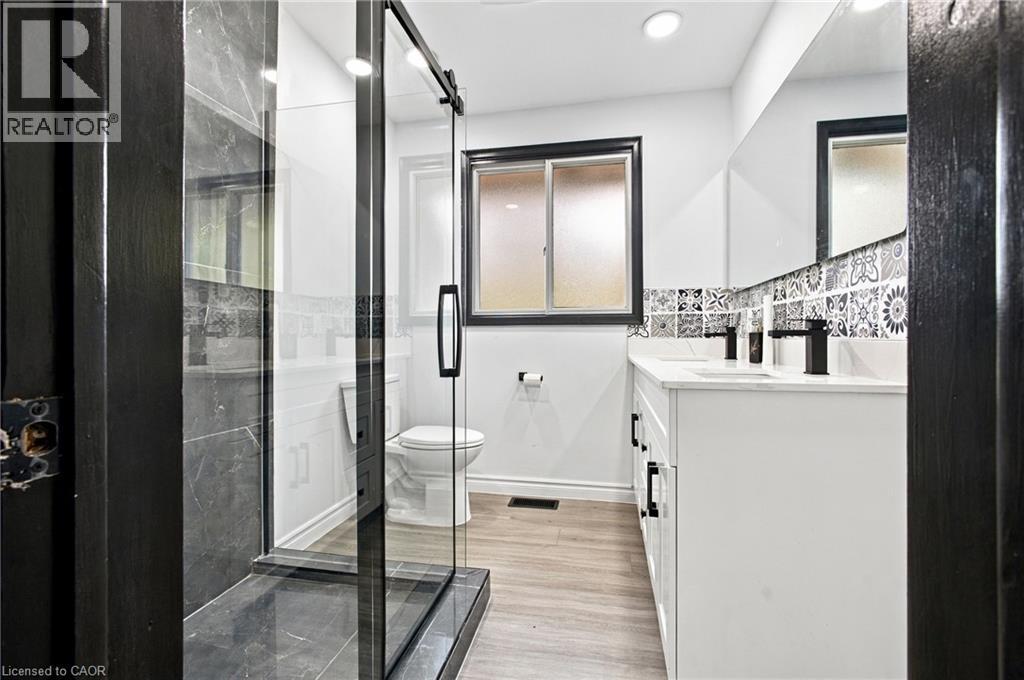 Dual vanity with white cabinetry and integrated sinks, matte black faucets, patterned tile backsplash, and a glass-enclosed shower with a black frame and dark tile surround - 246 Hillcrest Road, Cambridge, ON