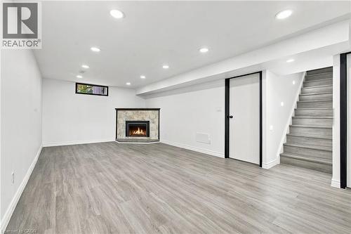 Recessed lighting, wood-finish flooring, corner fireplace with stone surround, a white door with black trim, and a staircase with recessed wall lighting - 246 Hillcrest Road, Cambridge, ON 