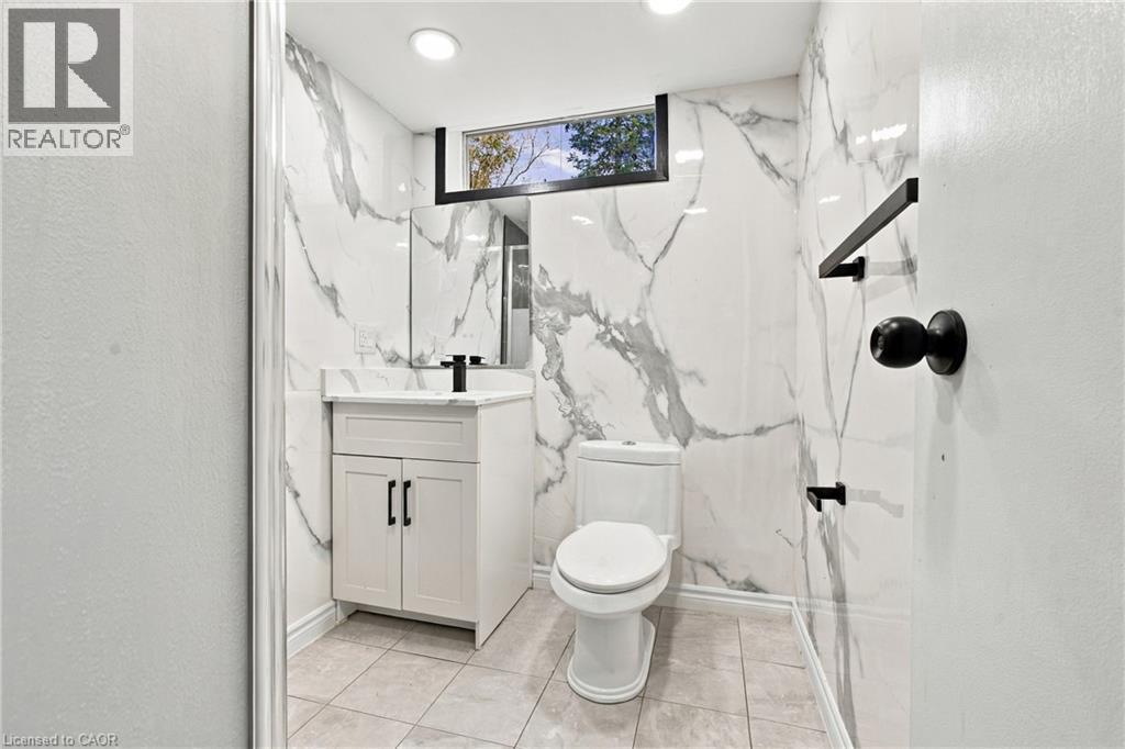 Modern bathroom featuring floor-to-ceiling marble-look wall tiling, a white vanity with a dark faucet, a recessed window, and recessed lighting - 246 Hillcrest Road, Cambridge, ON
