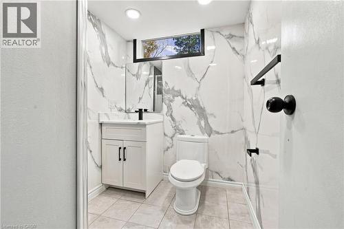 Modern bathroom featuring floor-to-ceiling marble-look wall tiling, a white vanity with a dark faucet, a recessed window, and recessed lighting - 246 Hillcrest Road, Cambridge, ON 