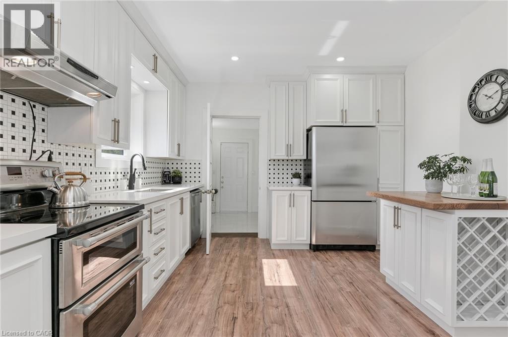 Kitchen featuring white cabinetry, stainless steel appliances, wood-finish flooring, a patterned tile backsplash, and a built-in wine rack - 164 Wilson Street, Hamilton, ON