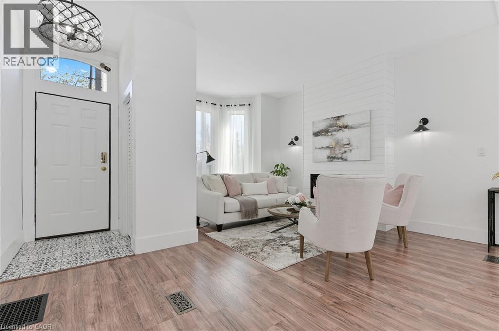 Bright open-concept living area featuring wood-finish flooring throughout, white shaker-style entry door with transom window, recessed ceiling lighting, and contemporary wall-mounted sconces - 164 Wilson Street, Hamilton, ON