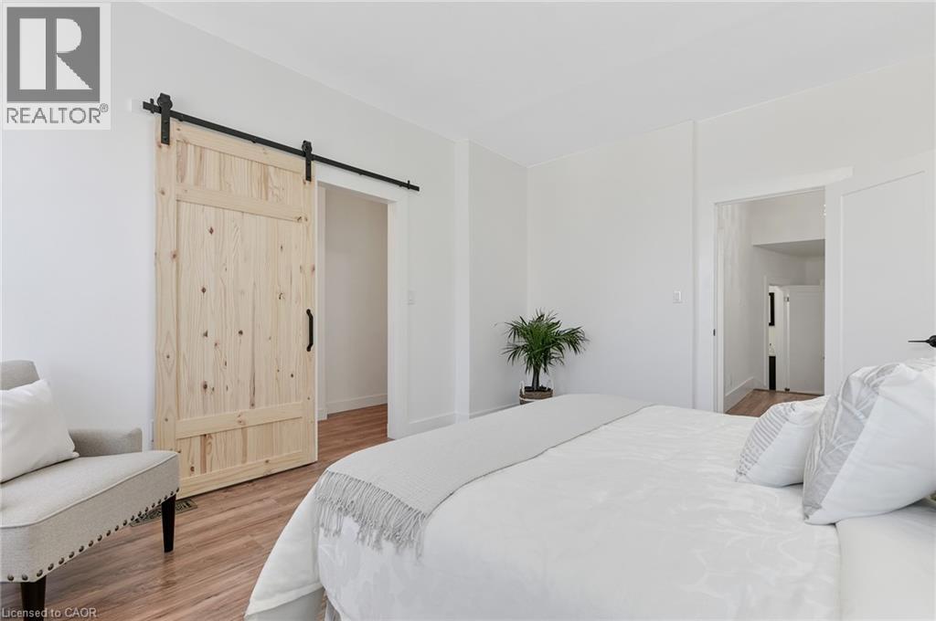 Wood-finish flooring throughout, white walls, and a natural wood barn door with black hardware - 164 Wilson Street, Hamilton, ON