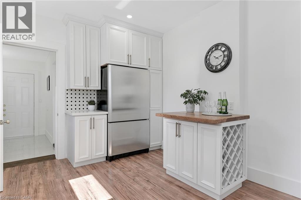 White shaker cabinetry, stainless steel refrigerator, patterned tile backsplash, wood-finish flooring, and a built-in wine rack - 164 Wilson Street, Hamilton, ON