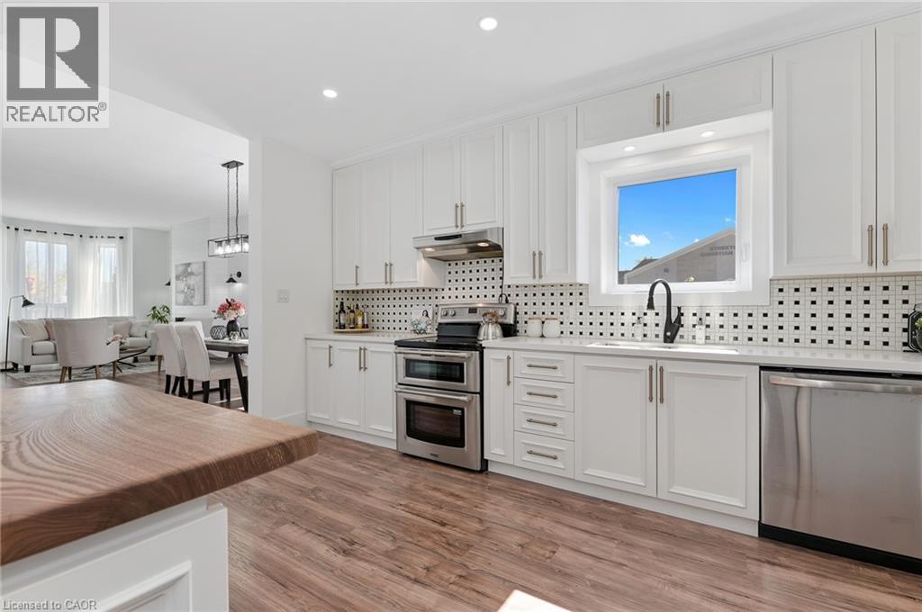 Contemporary kitchen featuring white shaker-style cabinetry, stainless steel appliances including double wall ovens and dishwasher, polished black countertops, geometric tile backsplash, and brushed n - 164 Wilson Street, Hamilton, ON