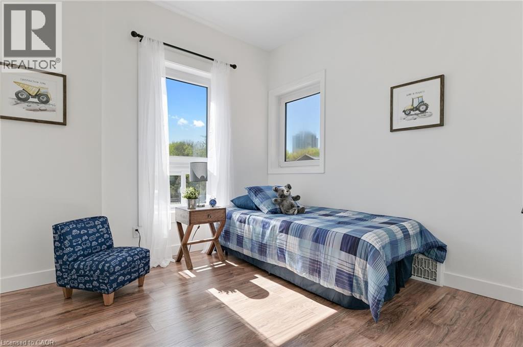 Bright secondary bedroom showcasing wood-finish flooring, dual windows with natural light exposure, and clean white walls - 164 Wilson Street, Hamilton, ON