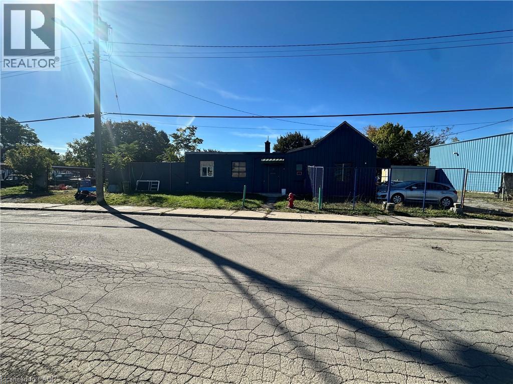 Single-story exterior with dark-toned vertical siding, a pitched roofline, and an enclosed fenced perimeter - 150 Princess Street, Hamilton, ON