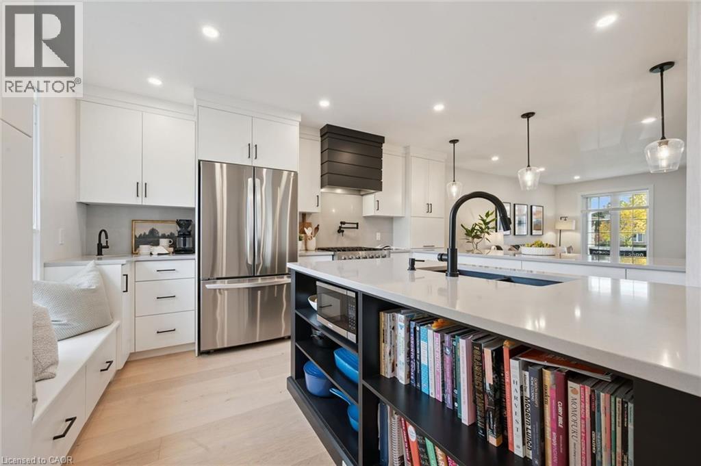 Gourmet kitchen with white cabinetry, stainless steel appliances, central island with built-in shelving, light wood-finish flooring, and recessed lighting - 6 Branwood Place, Kitchener, ON