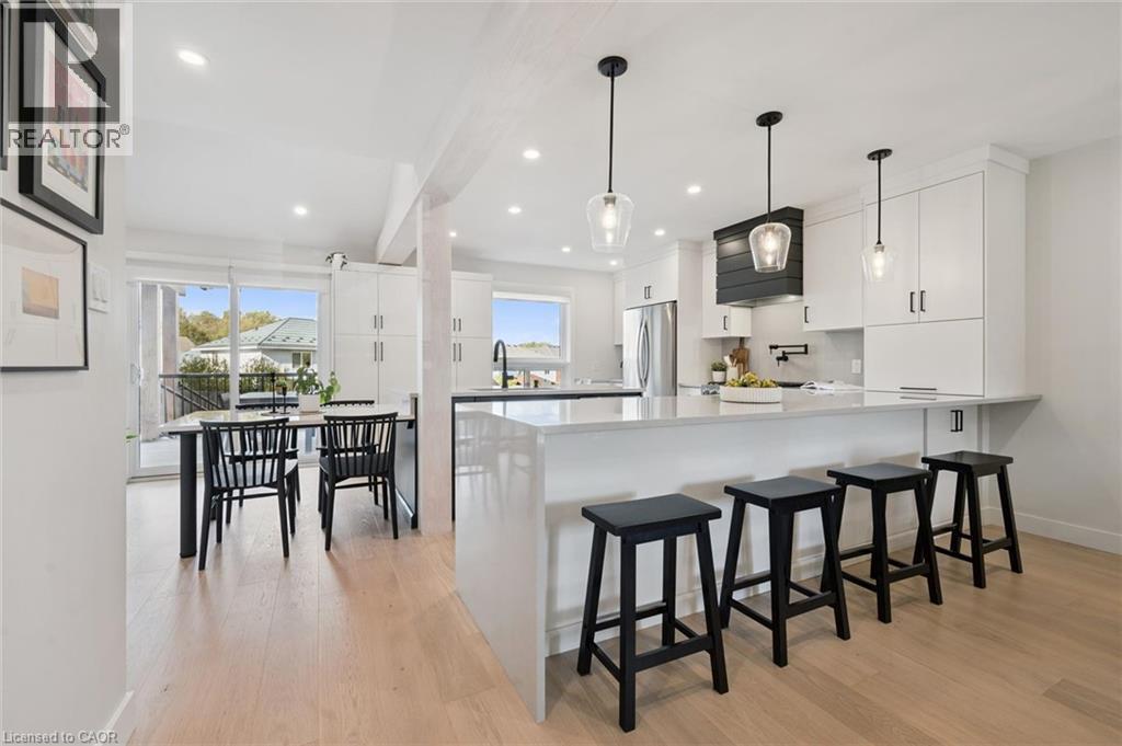 Open-concept kitchen and eat-in area featuring light-finish flooring, white cabinetry, a large kitchen island with counter seating, and pendant lighting - 6 Branwood Place, Kitchener, ON