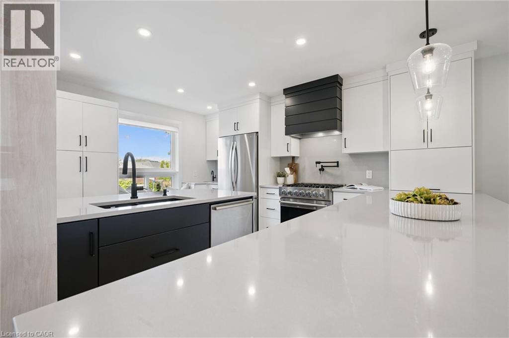 White cabinetry with black hardware, large kitchen island with light countertop, stainless steel refrigerator, stainless steel dishwasher, and a black range hood - 6 Branwood Place, Kitchener, ON