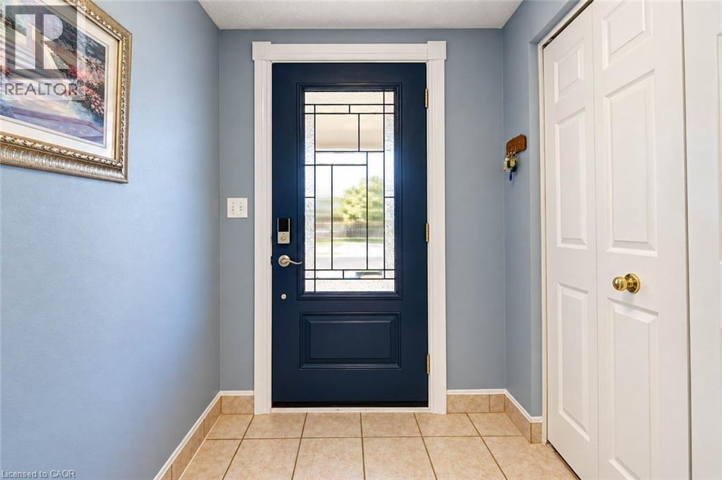 Entryway featuring a navy front door with decorative glass, tile flooring, and white bi-fold closet doors - 327 Oprington Place, Kitchener, ON