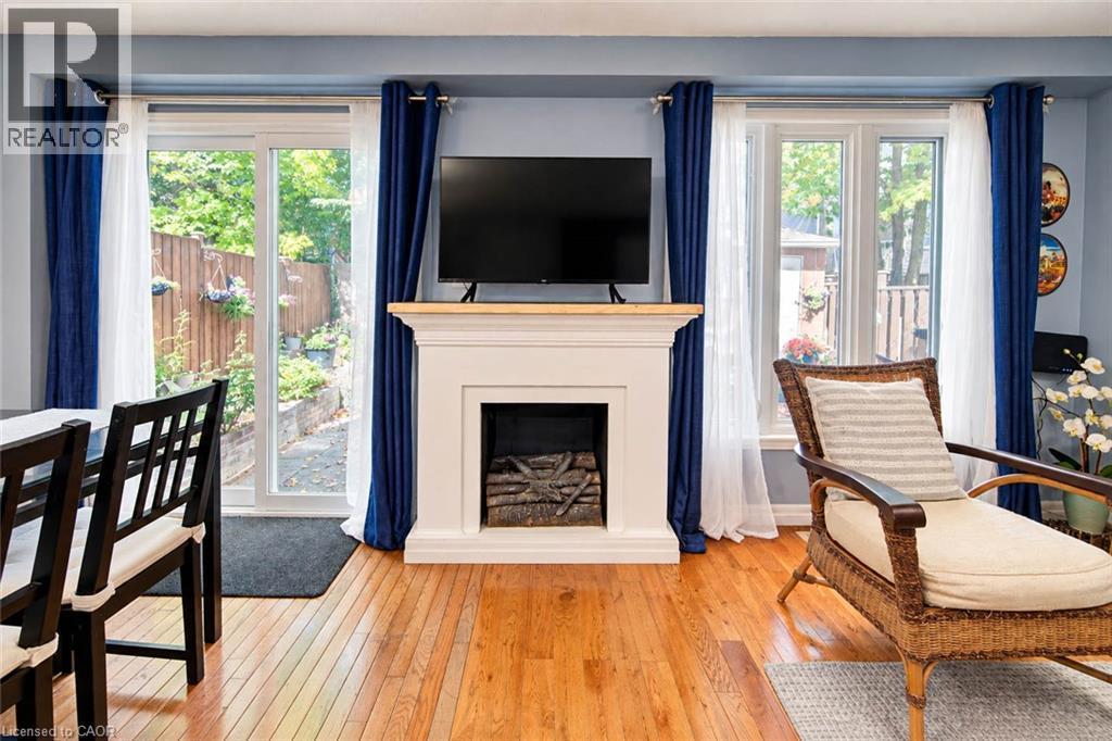 Hardwood flooring, a white mantelpiece with a wood-finish top, a fireplace insert, a sliding glass door, and a window - 327 Oprington Place, Kitchener, ON