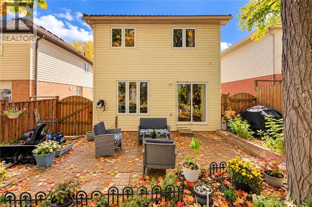 Rear exterior featuring light-colored siding, a paved patio, and a sliding glass door - 327 Oprington Place, Kitchener, ON