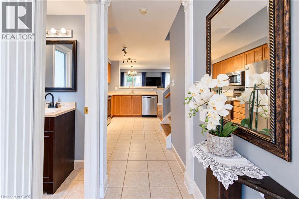 Tiled flooring throughout, dark wood-finish vanity with a light-toned countertop, black-finish faucet and framed mirror, stainless steel appliances, and wood-finish cabinetry - 327 Oprington Place, Kitchener, ON