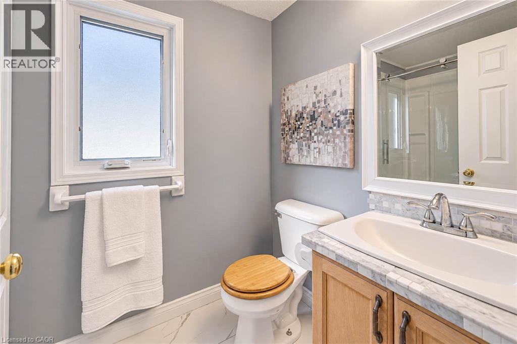 Single casement window, wood-finish vanity with chrome hardware, stone countertop, tile backsplash, and polished chrome faucet - 327 Oprington Place, Kitchener, ON