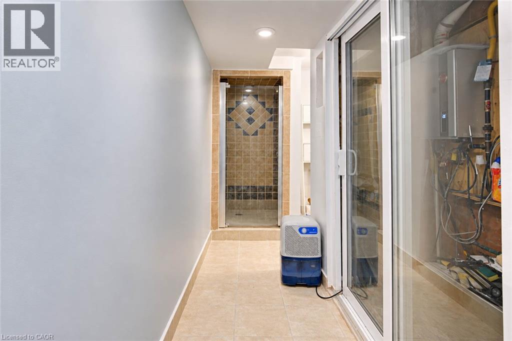 Recessed lighting illuminates the tiled flooring and shower with a glass enclosure, featuring decorative tile accents - 327 Oprington Place, Kitchener, ON
