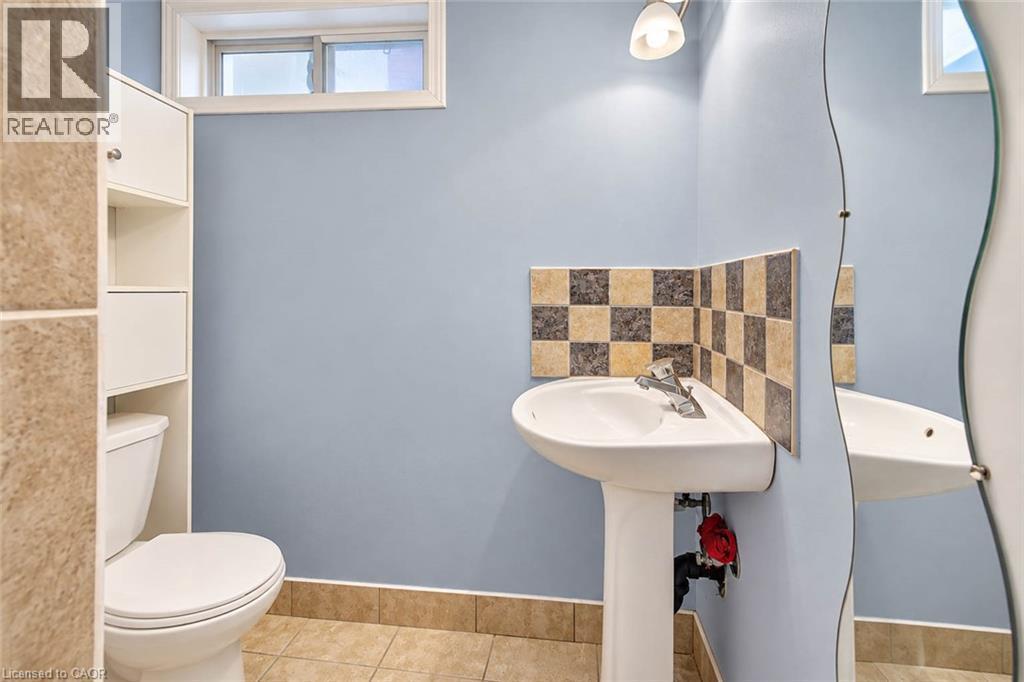 Pedestal sink with chrome faucet, checkerboard tile backsplash, and a wall-mounted curved mirror - 327 Oprington Place, Kitchener, ON