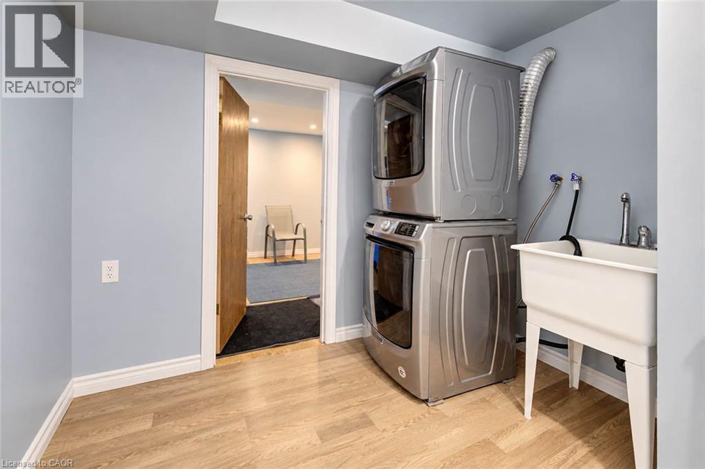 Laundry area featuring wood-finish flooring, light blue walls, a utility sink with faucet, and a stacked washer and dryer - 327 Oprington Place, Kitchener, ON