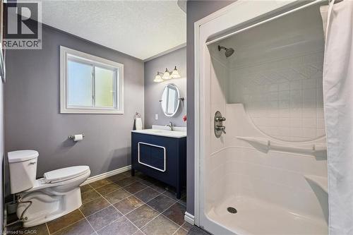 Full bathroom featuring a single-piece shower stall, dark blue vanity with a white countertop, oval mirror, three-light vanity fixture, and tiled flooring - 74 Selkirk Street, Cambridge, ON 