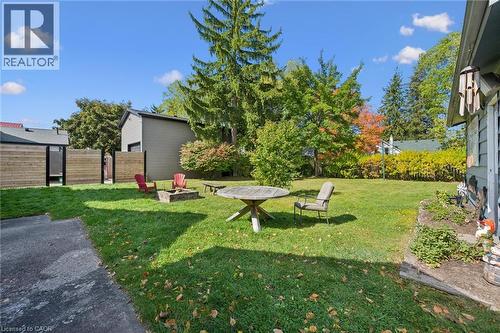 Expansive grassy area with mature perimeter trees, a built-in fire pit, and a horizontal wood fence - 74 Selkirk Street, Cambridge, ON 