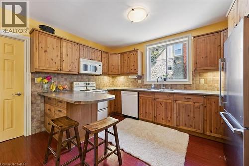 Wood-finish cabinetry, tile backsplash, built-in microwave, stainless steel refrigerator, and a double-basin sink - 74 Selkirk Street, Cambridge, ON 