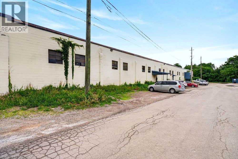 Single-story concrete masonry exterior featuring multiple window openings, metal canopy, and an expansive paved lot - 47 Head Street, Hamilton, ON