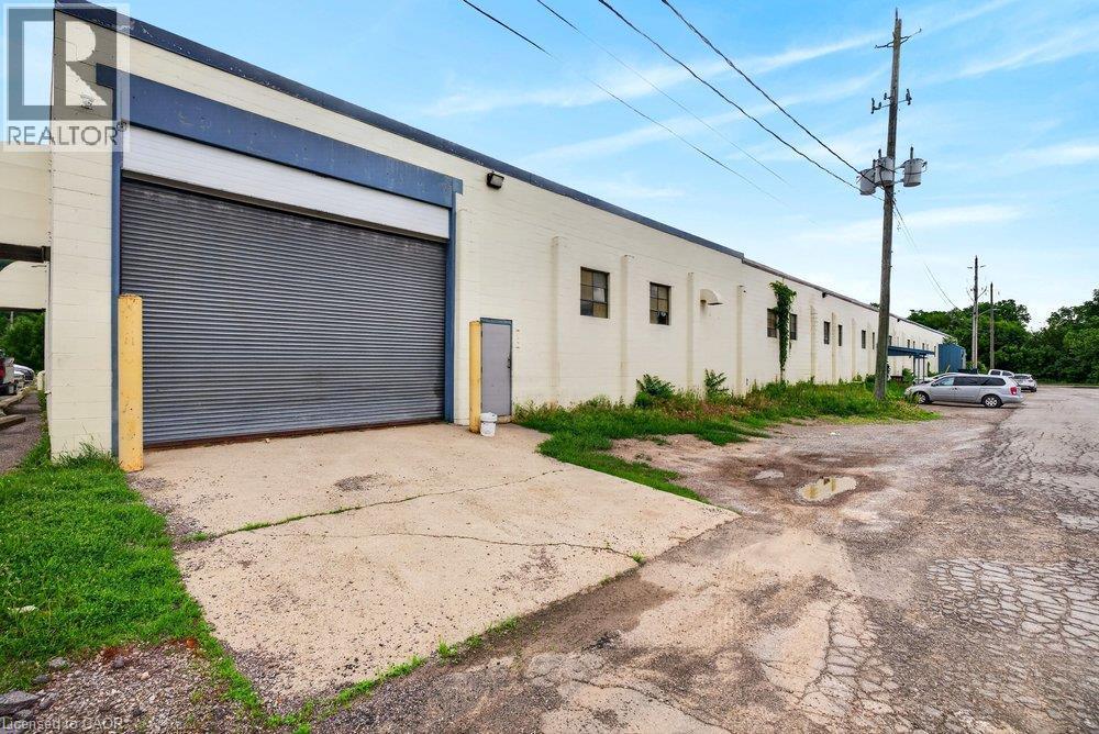 Industrial structure featuring a concrete masonry facade, a high-clearance metal roll-up door, and multiple exterior window placements - 47 Head Street, Hamilton, ON