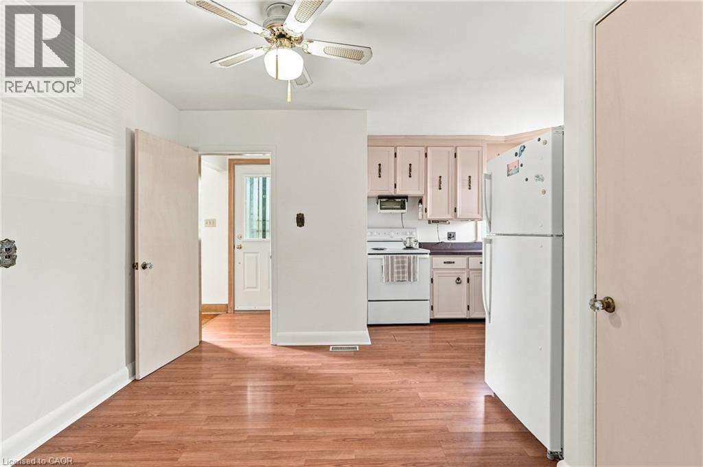 Kitchen area featuring wood-finish flooring, white cabinetry, an integrated ceiling fan with a light fixture, and an exterior door with a glass panel - 241 East 44Th Street, Hamilton, ON