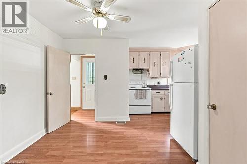 Kitchen area featuring wood-finish flooring, white cabinetry, an integrated ceiling fan with a light fixture, and an exterior door with a glass panel - 241 East 44Th Street, Hamilton, ON 