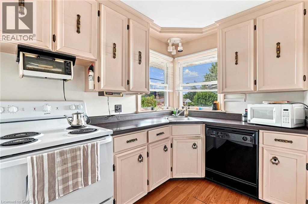 Kitchen featuring light-toned cabinetry, dark solid-surface countertops, wood-finish flooring, corner sink placement, and multi-pane windows - 241 East 44Th Street, Hamilton, ON