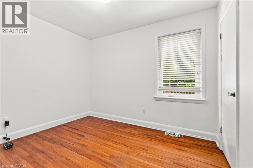 Room featuring wood-finish flooring, white walls, and a single-pane window with adjustable blinds - 241 East 44Th Street, Hamilton, ON
